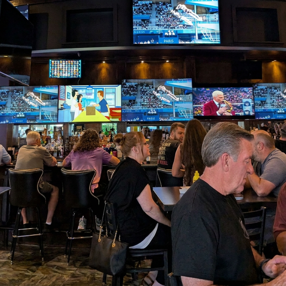 Busy sports bar with patrons seated at tables and numerous television screens showing sports and entertainment.