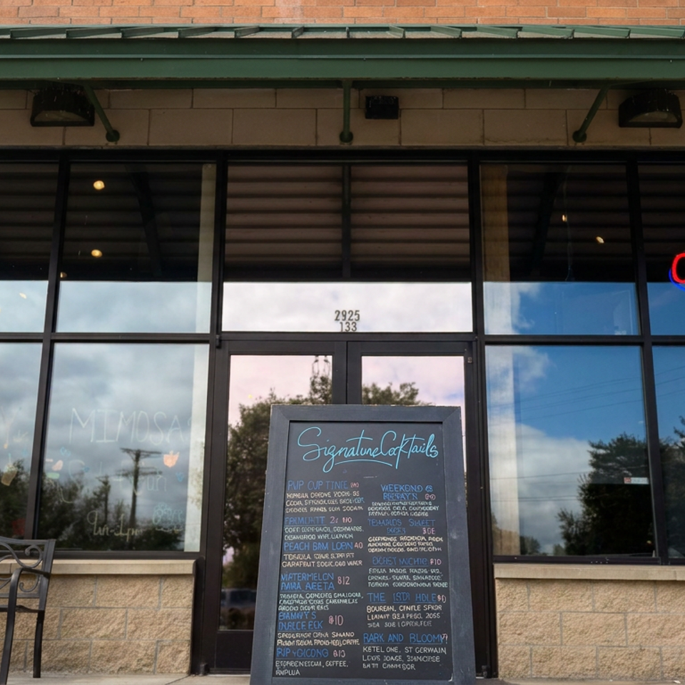 Restaurant storefront with an open sign, cocktail chalkboard, glass entrance, and decorative bench outside.